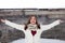 Girl spreads her arms in love and her white jacket forms a red heart in front of a wooden barn with lots of snow falling from the