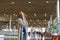 Girl standing in airport hall with valise and neck pillow.