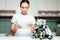 The girl is standing in the kitchen and holding a tablet. A small rhinoceros robot sits next to the table.