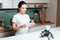 The girl is standing in the kitchen and holding a tablet. A small rhinoceros robot sits next to the table.