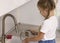 Girl is standing by the kitchen sink washing dishes