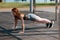 A girl standing in a pose for push up. Fitness class. The female is exercising in the park