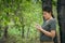 The girl is standing, taking notes in a small note book in the green forest