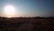 A girl stands alone on a dirt road, between dried fields