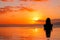 A girl stands with her back in the pool and looks at the setting sun in the ocean