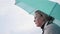 A girl stands under a green umbrella on the river Bank. Side view