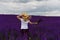 A girl in a straw hat with a bouquet of wildflowers runs along a lushly blooming lavender field