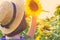 Girl in straw hat holding beautiful sunflower against sunflower field as natural background. Agricultural and harvesting concept.