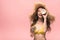 Girl in straw hat holding coconuts isolated on pink