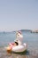 Girl in a straw hat lies on an inflatable white unicorn in the water near the sea shore
