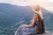 Girl in straw hat sits on top hill and looks out at mountains. Calm rest and relaxation concept