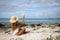 The girl in straw hat sitting on the beach with big seashell in the hand.