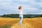 Girl in straw hat stands on a haystack on a bale in the agricultural field after harvesting