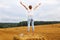 Girl with straw hat stands on a haystack on a bale in the agricultural field after harvesting