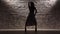 Girl in striped dress dancing twerk against the light brick wall. Silhouette. Slow motion