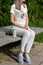 Girl in striped pants and blue shoes sitting on a wooden bench next to a cup of coffee and sunglasses in the park on spring sunny