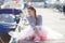 A girl in a striped sailor`s t-shirt and pink skirt sits alone on a wooden pier near the sea and boats