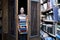 Girl student holds a large stack of books and carries a lot of literature in the library, she is preparing for study, the seller