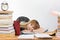 Girl student lay behind desk crammed with books and papers