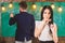 Girl student play with eyeglasses while teacher writes on chalkboard. Lady on dreamy face not pay attention to teacher