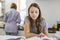 Girl studying at table with mother standing in background