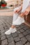 Girl in stylish jeans sits and ties the shoelaces on the white fashion shoes on the street