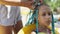 A girl in a suit weaves African braids in her hair on a sunny day