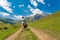 A girl with a suitcase walks along a dirt road in the mountains. Interesting jouney of lonely woman