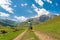 A girl with a suitcase walks along a dirt road in the mountains. Interesting jouney of lonely woman