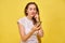 A girl in summer clothes stands on a yellow background and listens to music in wireless headphones through a smartphone switching