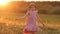 A girl in a summer dress spins on a field at sunset