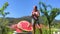 a girl in a summer sports outfit bites a watermelon against the backdrop of mountains she is out of focus in the