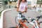 Girl summer stands bicycle, activates application buying rental bicycle in parking lot, in hands of phone. Online