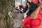 A girl in sunglasses, a headscarf and a red jacket helps a British cat in a pom-pom hat climb a tree