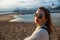 A girl in sunglasses stands on the Santa Monica beach with a background of the setting sun and pier