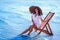 girl in sunhat and tunic sitting on the beach chair at seaside while holds cocktail. Summer vacation