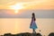 A girl at sunset looks at the sea from a high cliff.