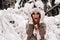 A girl in a sweater and mittens in winter holds her head with her hands in a snowy forest