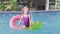 girl in swimming pool, child having fun, sitting on pink donut swimming ring, playing under water. Summer travel family