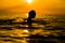 Girl swimming in the sea at sunset, splashes of transparency water, female black silhouette