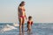 A girl in a swimsuit runs with a toddler on the beach with shells on the background of the sea with waves