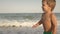 A girl in a swimsuit runs with a toddler on the beach with shells on the background of the sea with waves