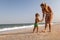 A girl in a swimsuit runs with a toddler on the beach with shells on the background of the sea with waves