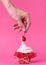 Girl takes cherry from the cake spread with cream. the concept of sexual pleasures. pink background, studio shooting