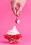 Girl takes cherry from the cake spread with cream. the concept of sexual pleasures. pink background, studio shooting