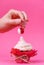 Girl takes cherry from the cake spread with cream. the concept of sexual pleasures. pink background, studio shooting