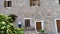 Girl taking picture with smart phone in the old town with stone facade of a house and wood windows. White sweater in mediterranean