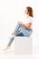 Girl teenager in blue jeans sits on cube in white studio