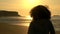Girl teenager female young woman with curly hair standing on a beach looking at sunset or sunrise