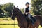 Girl teenager jockey sits on a brown horse in nature.